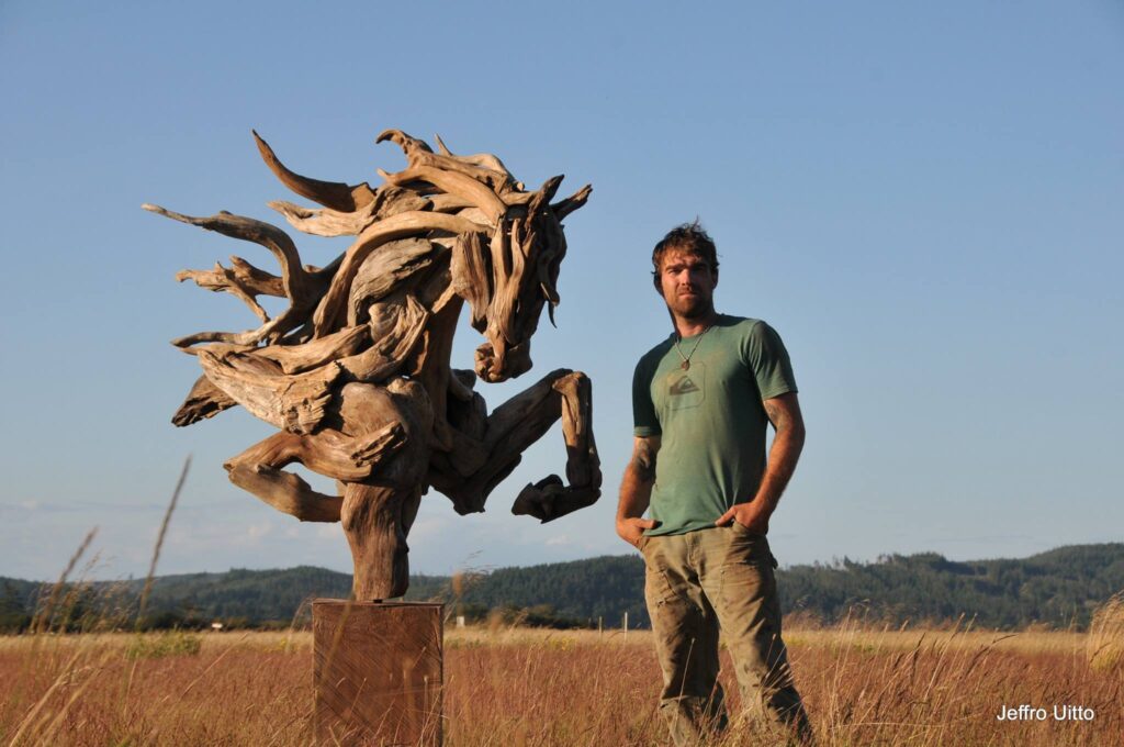 Artist Jeffro Uitto standing with his driftwood horse sculpture
